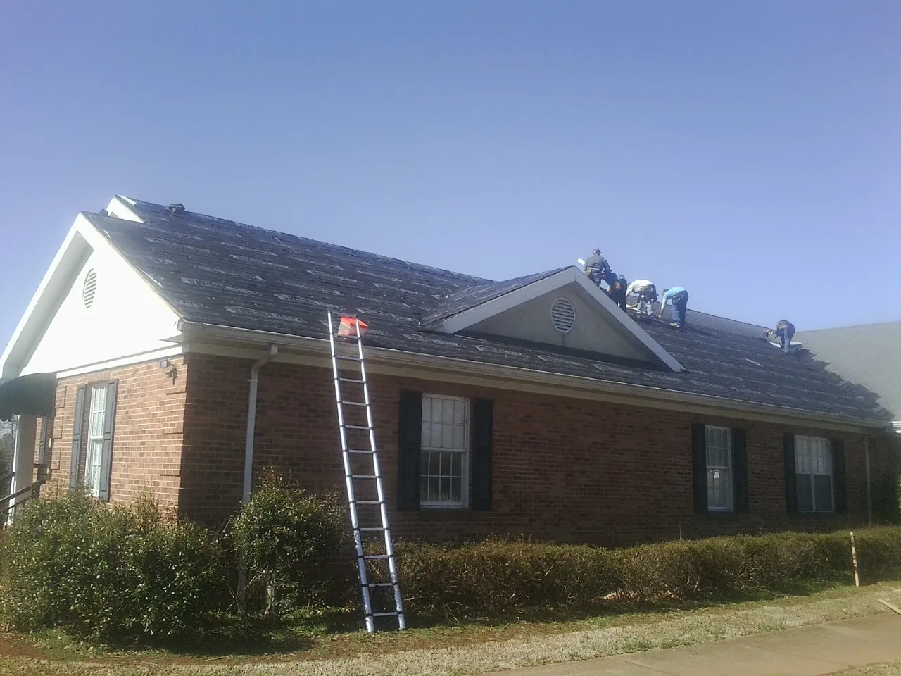 Crew tearing shingles off a brick ranch roof with a ladder set — Emergency Roof Repair work by our crew in Saltillo