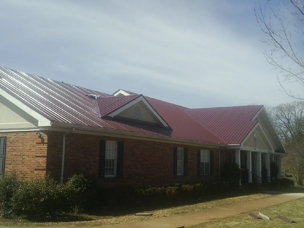 Red metal roof with gabled entries on a long brick building, from a Hail Damage Roof Repair job in Saltillo