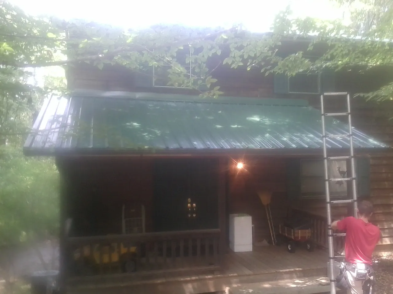 Worker on a ladder at the green porch roof of a wooded cabin in Saltillo