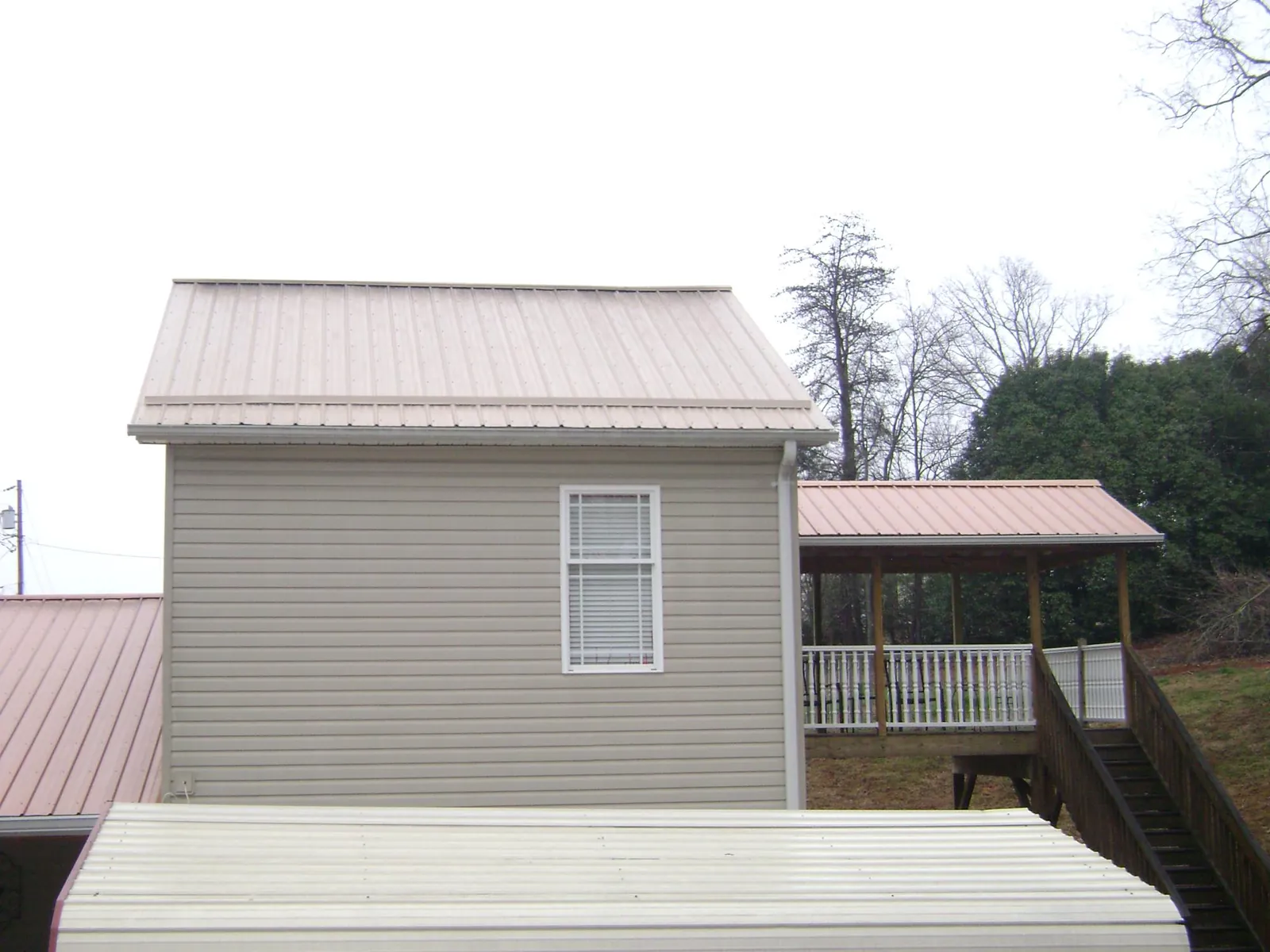 Tan metal roofs on a two story addition and attached porch, from a Roof Replacement job in Saltillo